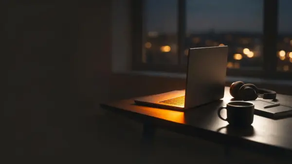 Laptop mit warmem Lichtschein, Kopfhoerer und Tasse am Abend